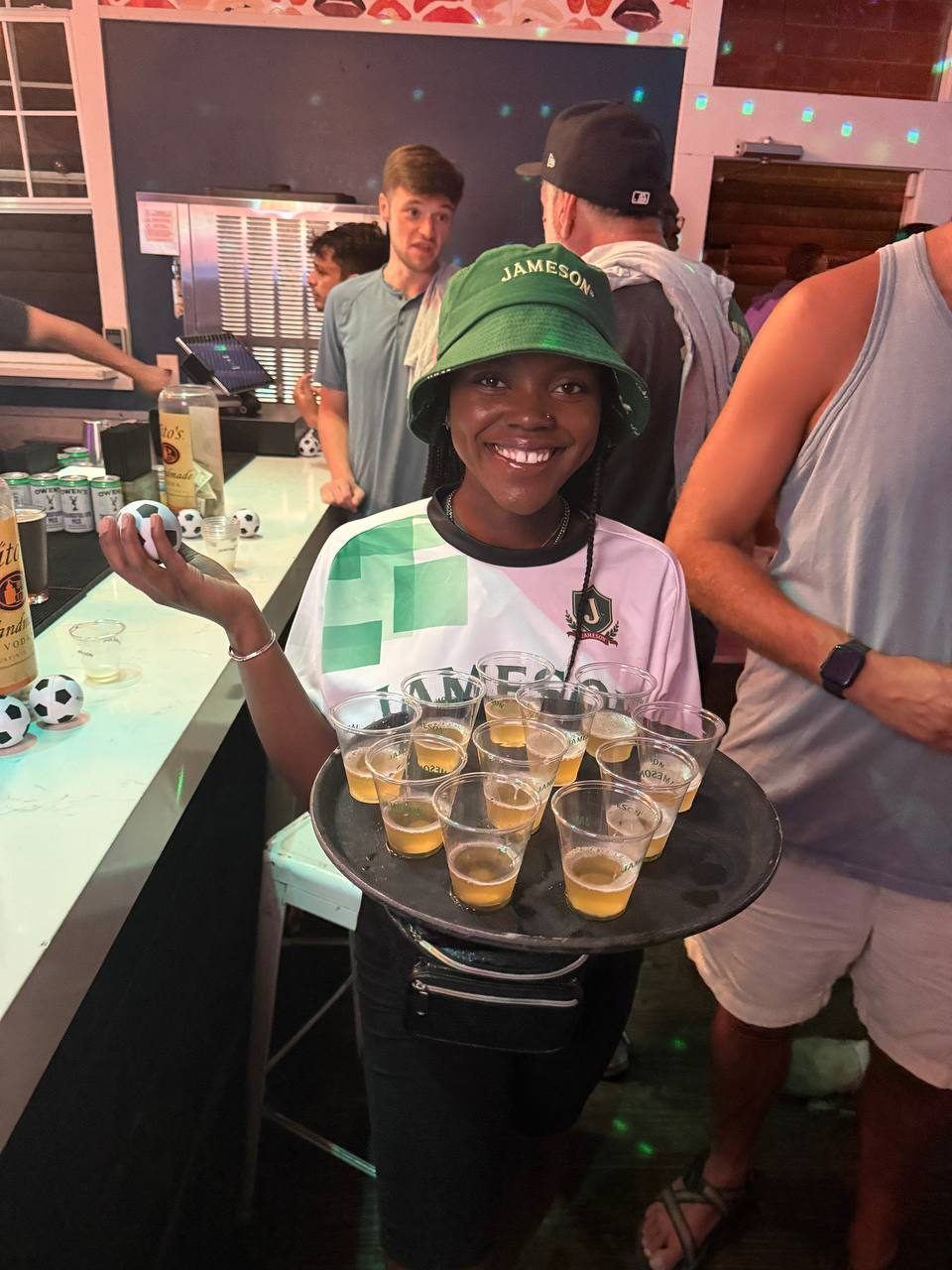 Events — Jameson brand ambassador in branded bucket hat serving a tray of drink samples at a soccer watch party bar