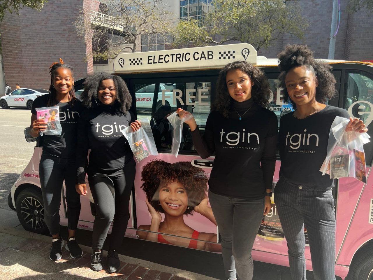Events — Four tgin brand ambassadors handing out haircare sample bags beside a pink Electric Cab shuttle