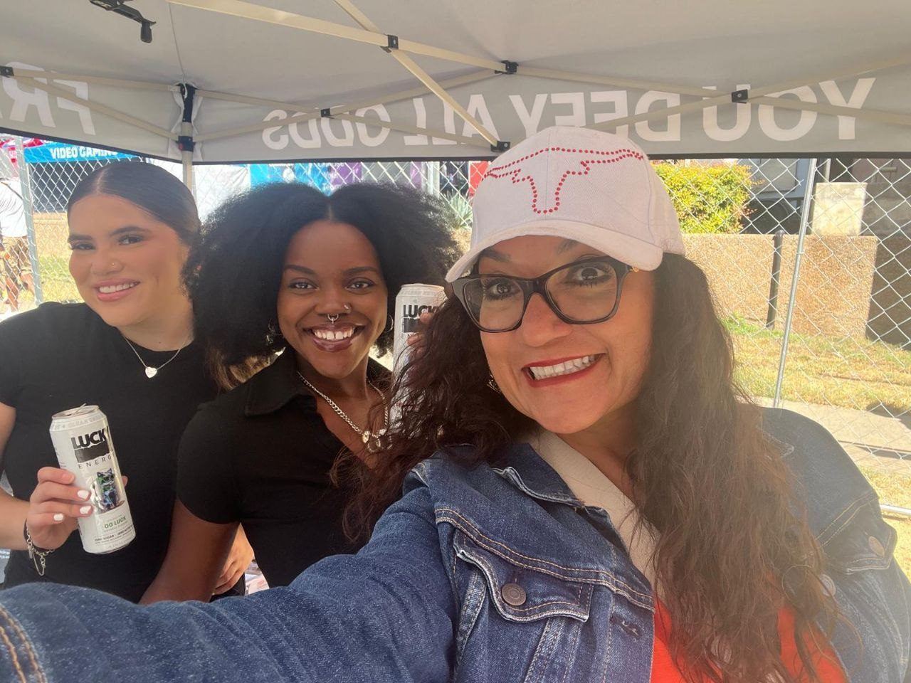 Events — Two Lucky Energy brand ambassadors holding cans posing for a selfie with a guest under a branded tent