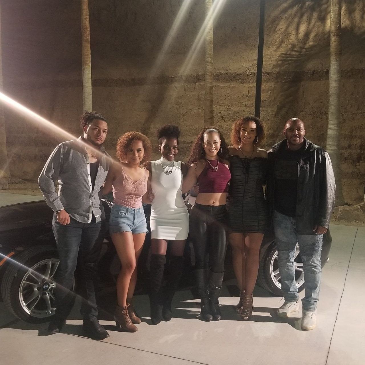 Events — Six-member ambassador team posing beside a black sports car at a nighttime palm-lined venue