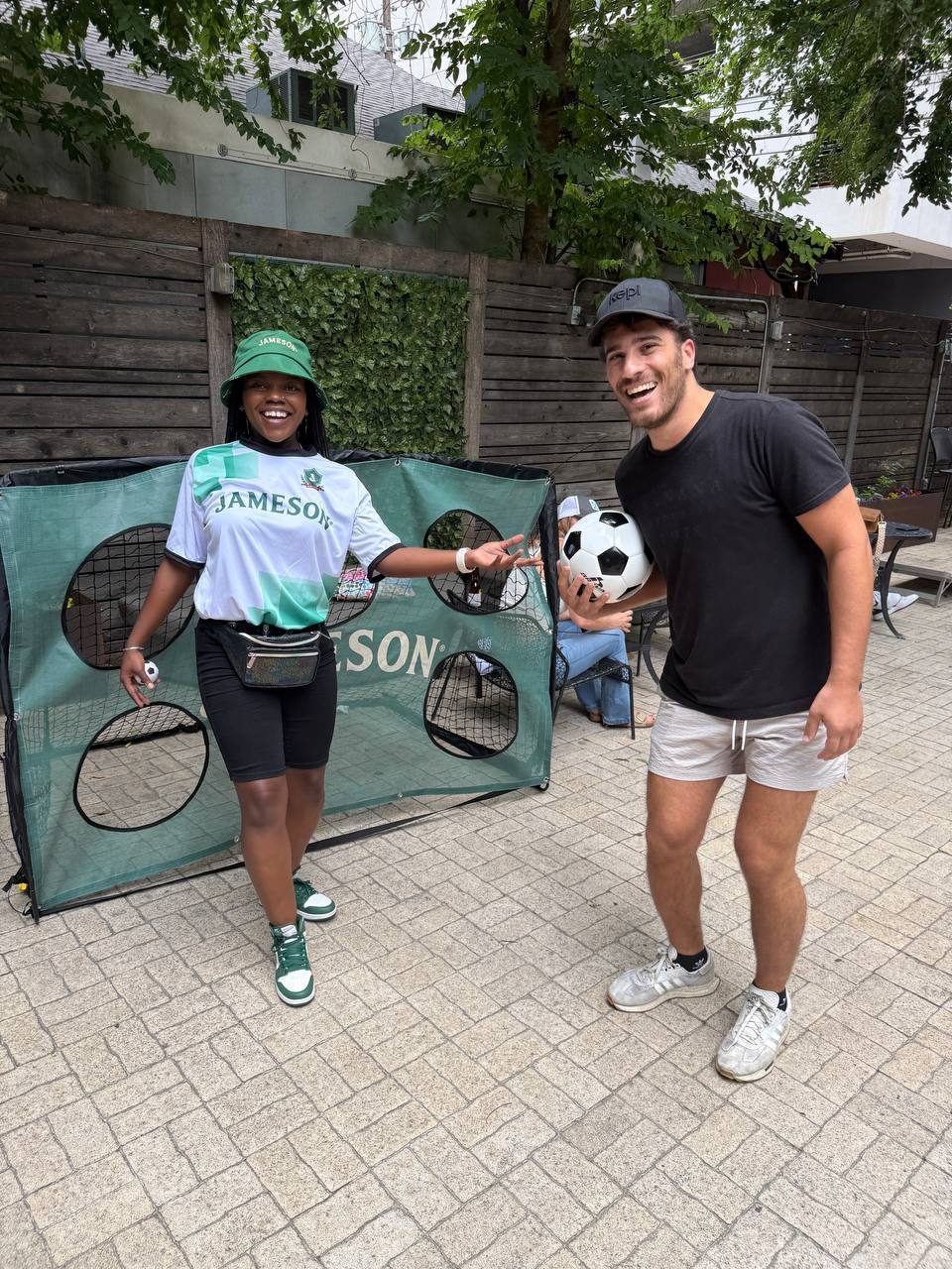 Events — Jameson brand ambassador and smiling guest holding a soccer ball at the branded target goal on a bar patio