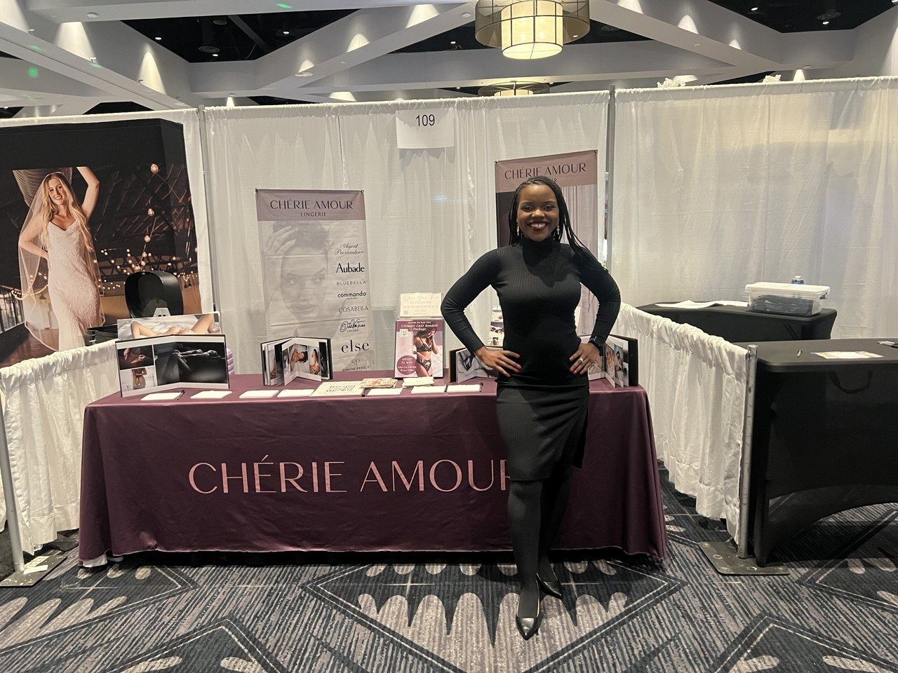 Events — Chérie Amour Lingerie ambassador at the booth 109 bridal expo table with boudoir portfolio displays and the brand banner