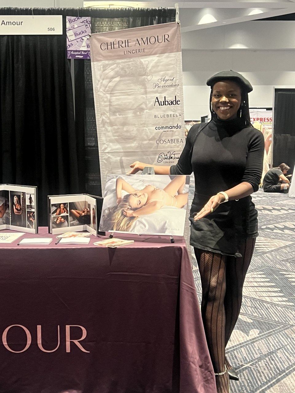 Events — Chérie Amour ambassador in a beret presenting a boudoir print at the booth 506 lingerie display