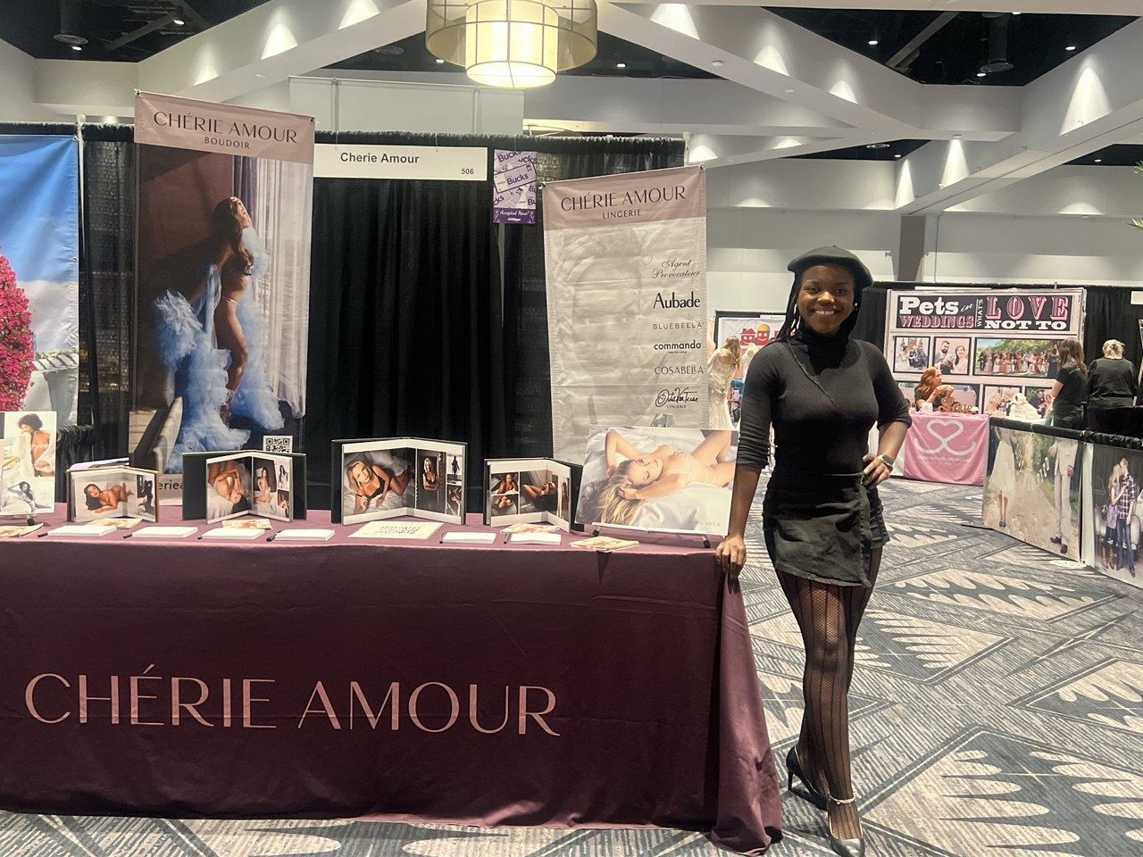 Events — Chérie Amour ambassador beside the full booth 506 spread of boudoir albums and Lingerie and Boudoir brand banners