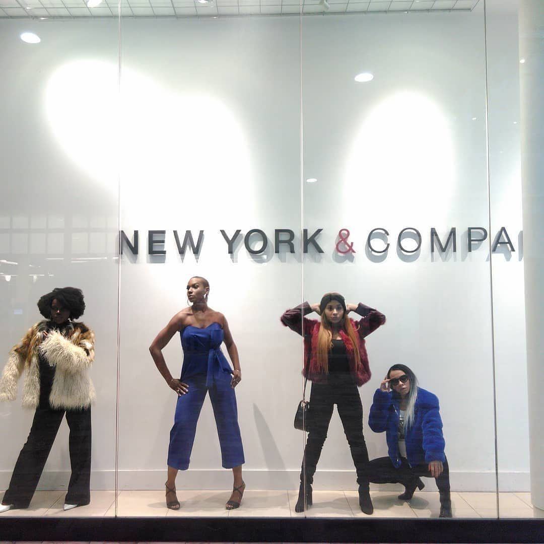 Fashion Showcase — Four models striking poses in fur jackets and a blue jumpsuit inside a New York & Company window display