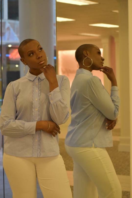 Fashion Showcase — Model in a light blue scalloped blouse and white pants posing beside a mirror reflecting her profile