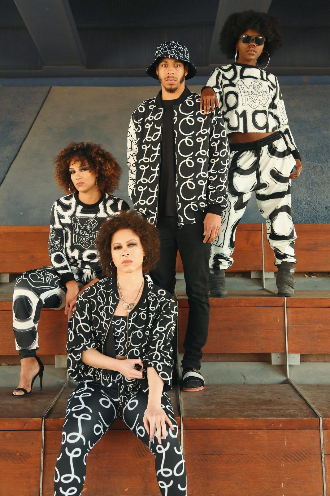 Fashion Showcase — Four models in coordinated black-and-white graffiti-print streetwear posing on tiered amphitheater benches outdoors