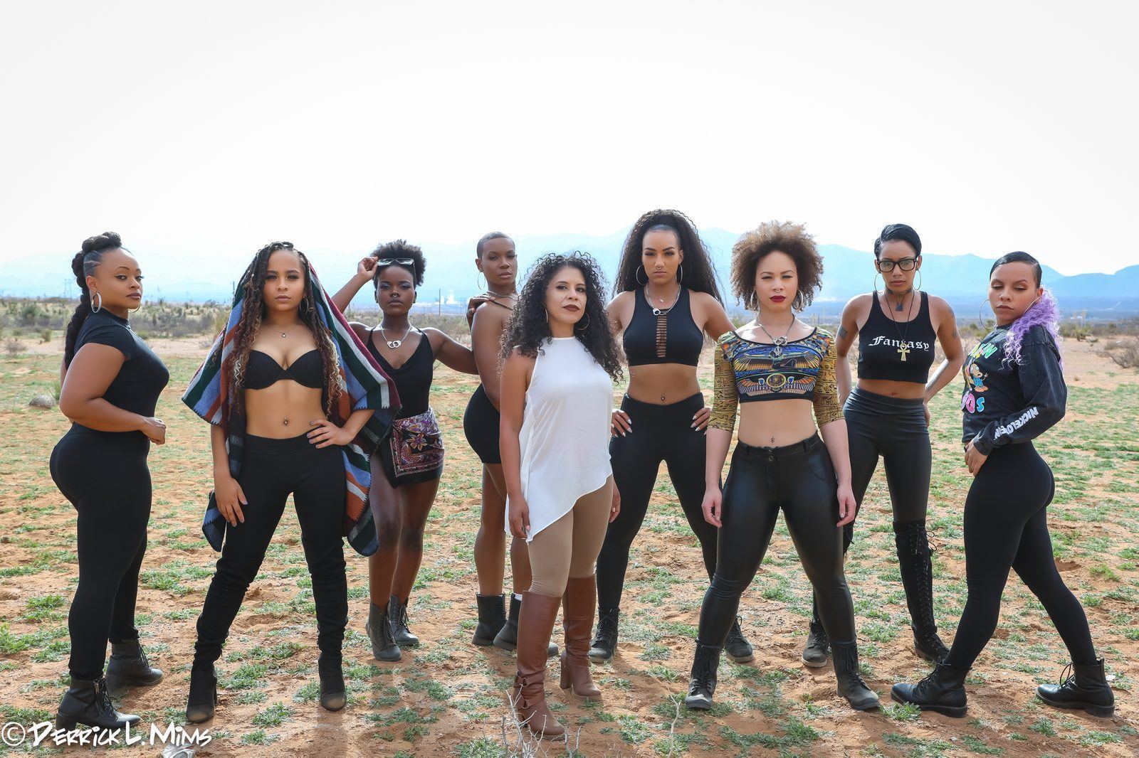 Fashion Showcase — Nine models in coordinated black looks standing in formation across a desert landscape with mountains behind