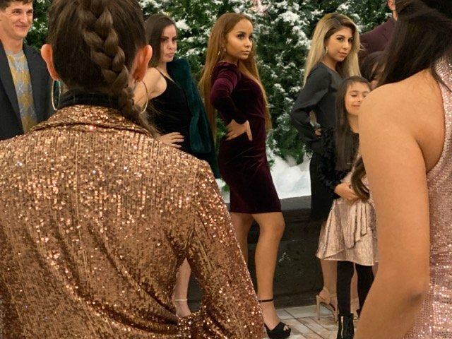 Fashion Showcase — Models in velvet and sequined holiday looks lining up beside snow-flocked Christmas trees at an event