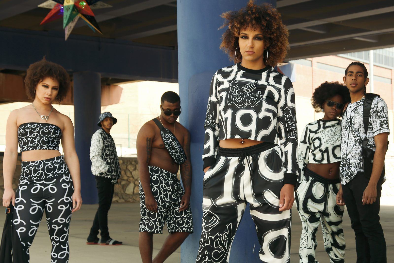 Fashion Showcase — Six models showcasing matching black-and-white graffiti-print streetwear beneath a highway overpass
