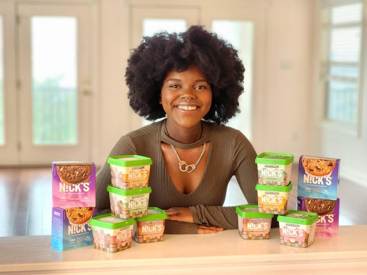 Influencer Work — Creator smiling behind a counter stacked with Nicks ice cream pints and cookie boxes in a sunlit room