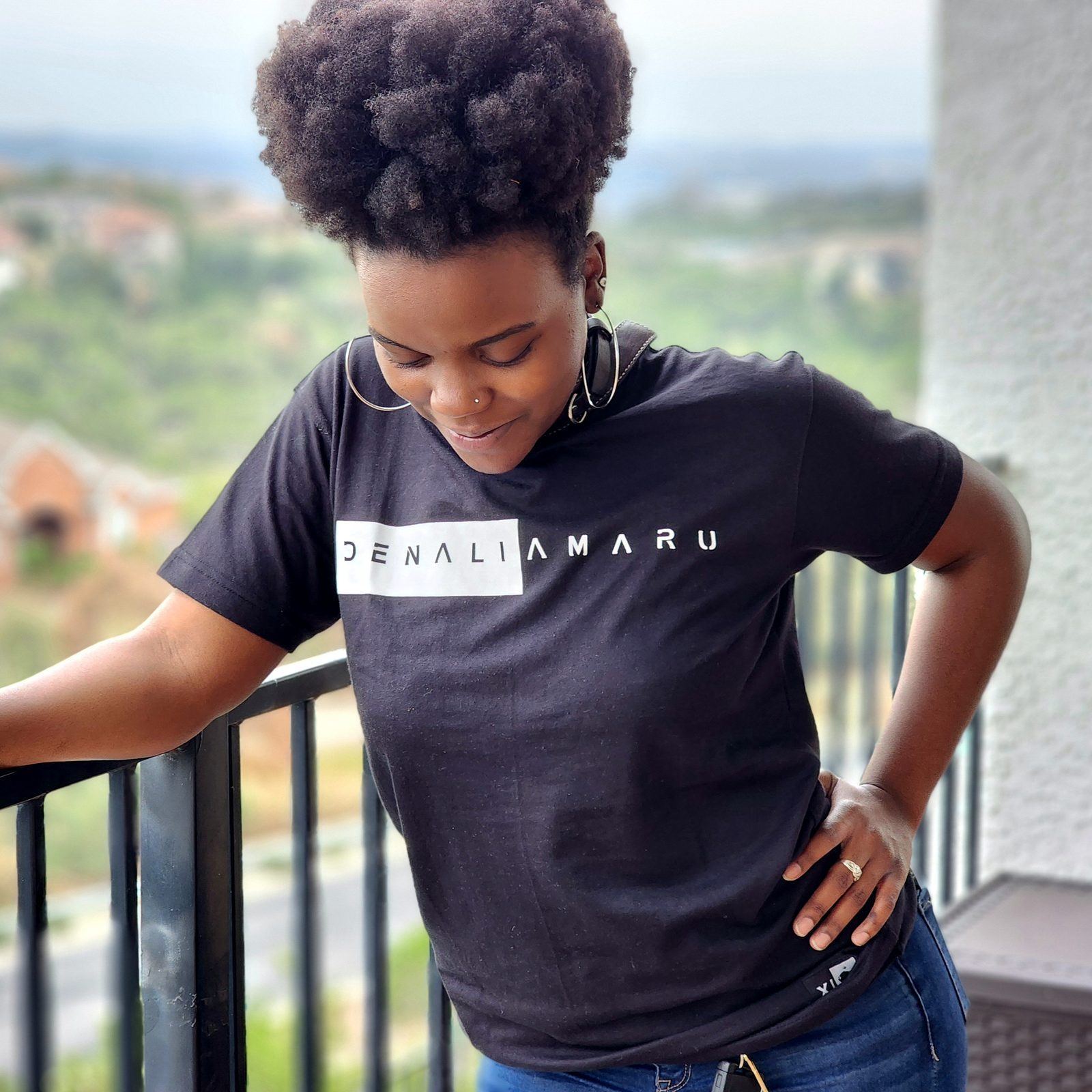 Influencer Work — Creator modeling a Denali Amaru tee on a balcony overlooking a hillside neighborhood, hand on hip