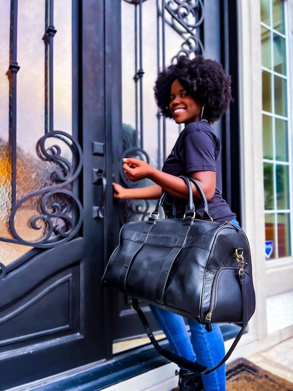 Influencer Work — Smiling creator with a black leather duffel on her arm opening an ornate wrought-iron front door