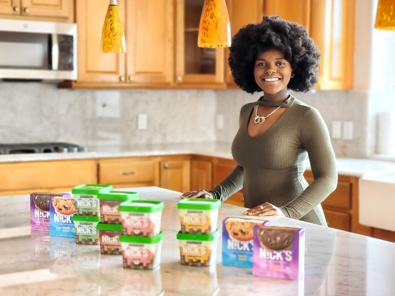Influencer Work — Creator in an olive dress presenting Nicks ice cream pints and cookie boxes on a marble kitchen island
