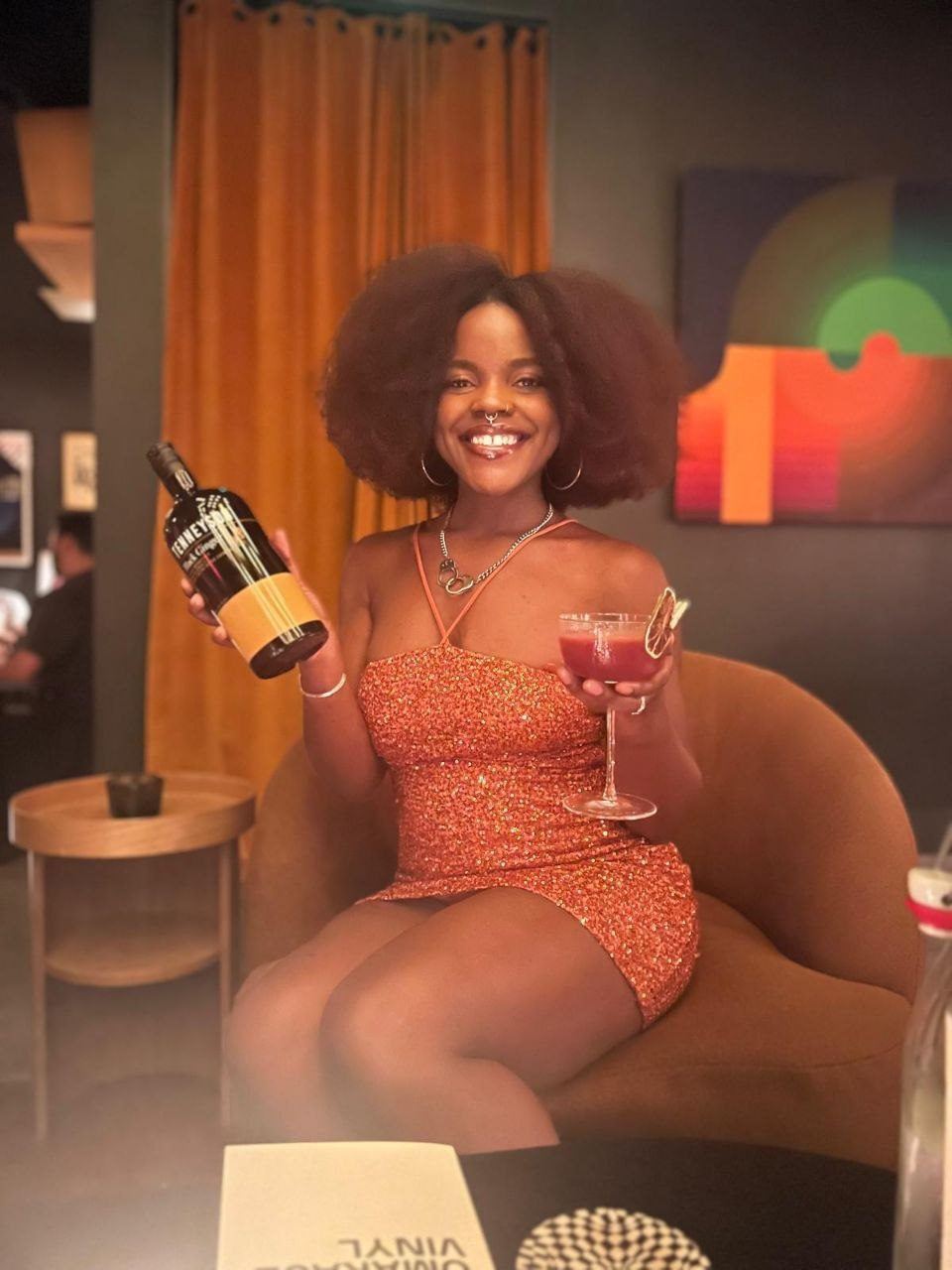 Influencer Work — creator holding a bottle and cocktail against a warm curtain backdrop