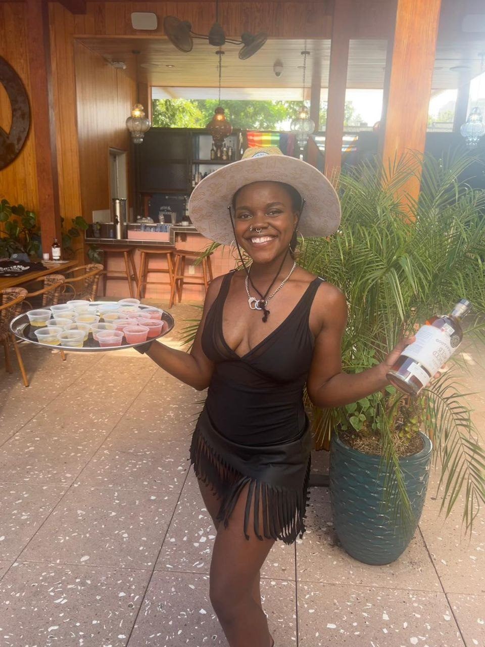 Influencer Work — creator in wide-brim hat presenting a bottle in a plant-filled patio setting