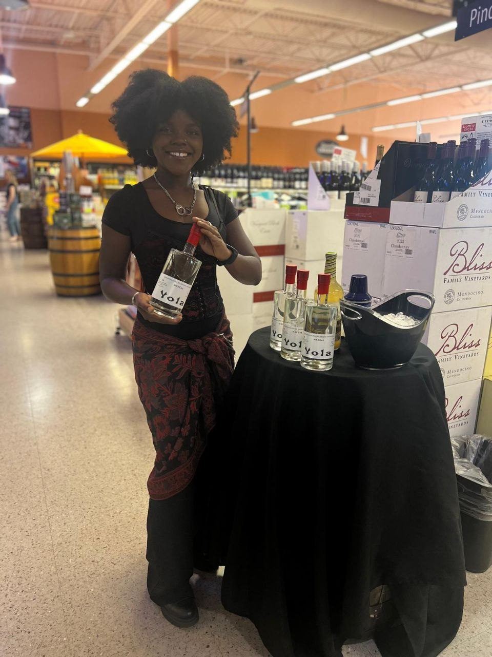 On-Site Activations — Brand ambassador presenting Yola Mezcal at a draped tasting table beside stacked Bliss Family Vineyards wine cases