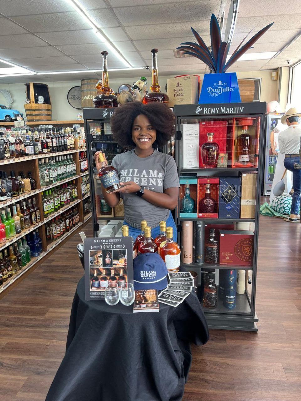 On-Site Activations — Milam & Greene whiskey tasting with branded ambassador, table signage, and cap beside a Remy Martin display