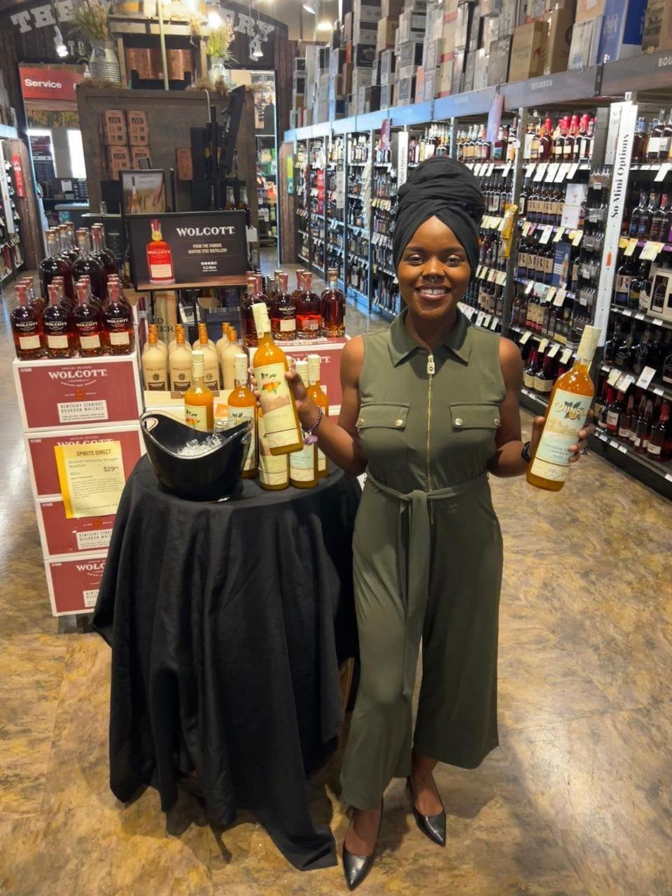 On-Site Activations — Brand ambassador presenting bottled cocktails at a draped table beside a Wolcott Kentucky Straight Bourbon display