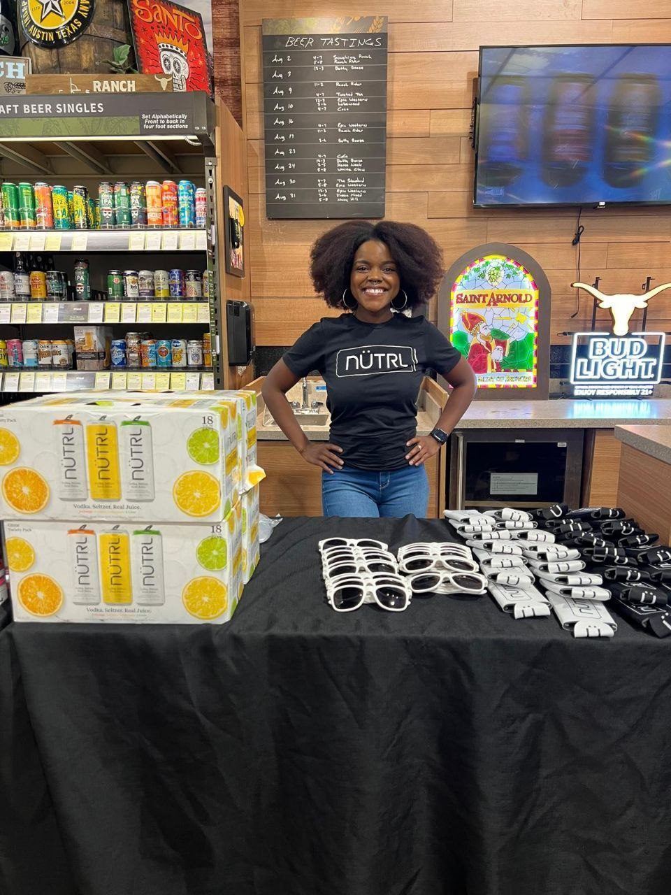 On-Site Activations — NUTRL vodka seltzer sampling with branded ambassador, variety packs, sunglasses, and koozies by a beer tastings chalkboard