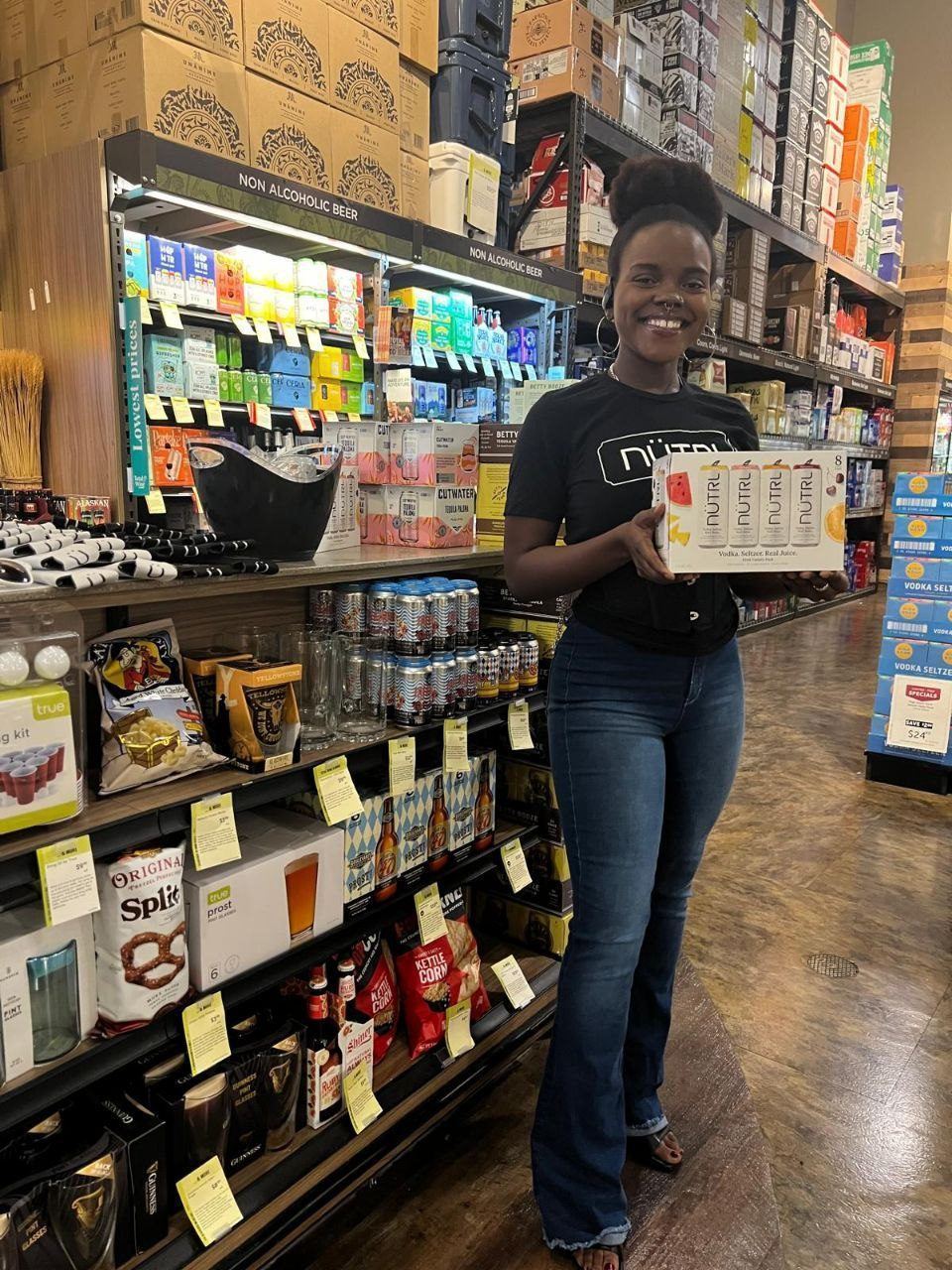 On-Site Activations — NUTRL ambassador holding a vodka seltzer variety pack in a grocery beer aisle near Cutwater displays