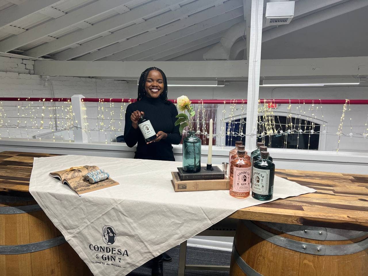 On-Site Activations — Condesa Gin tasting with ambassador presenting bottles on a branded cloth under string lights in a loft venue