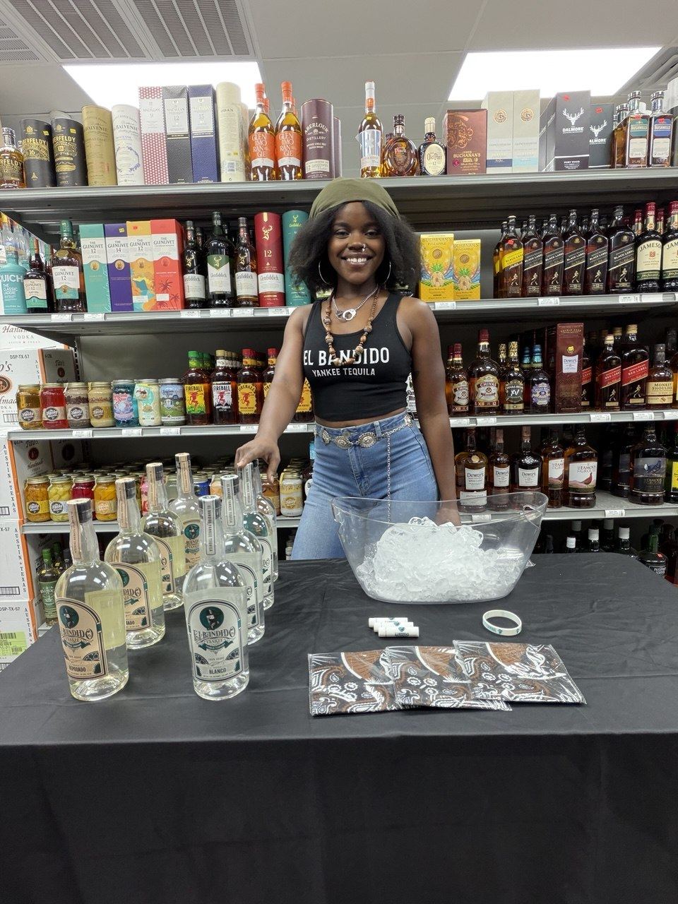 On-Site Activations — El Bandido Yankee Tequila ambassador at a liquor store tasting table with Blanco and Reposado bottles, branded bandanas, and lip balms