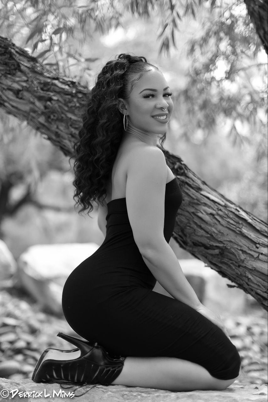 Photography — Black-and-white outdoor portrait of a model in a strapless dress kneeling beside a leaning tree trunk