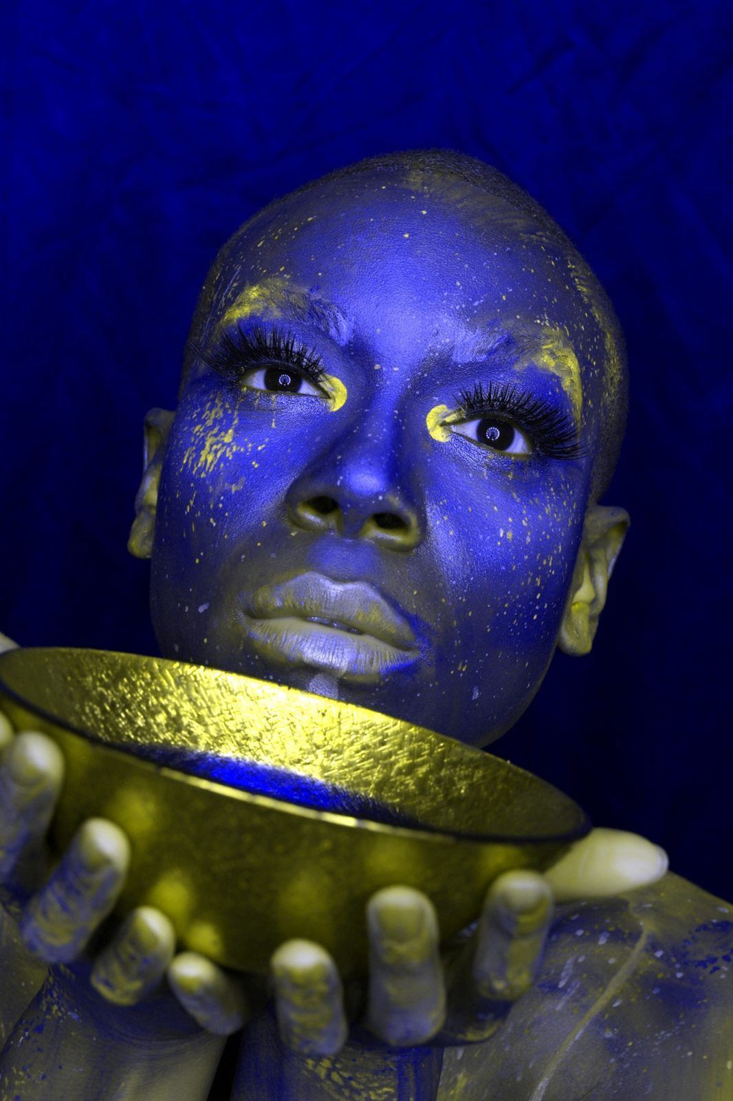 Photography — Creative studio portrait of a model in blue body paint with gold flecks holding a gilded bowl