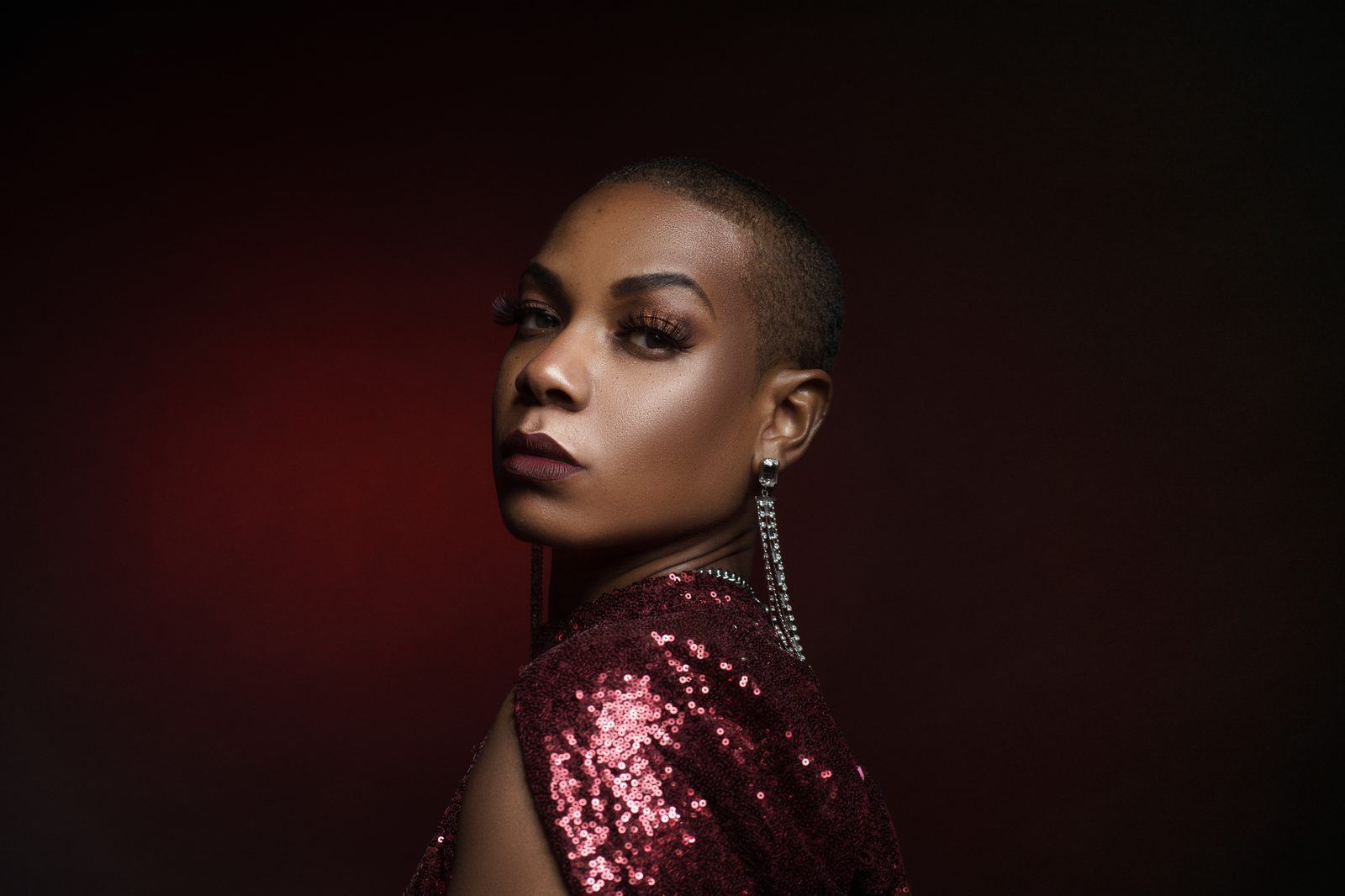 Photography — Model in a deep red sequin dress glancing over her shoulder with a long rhinestone earring, moody studio lighting