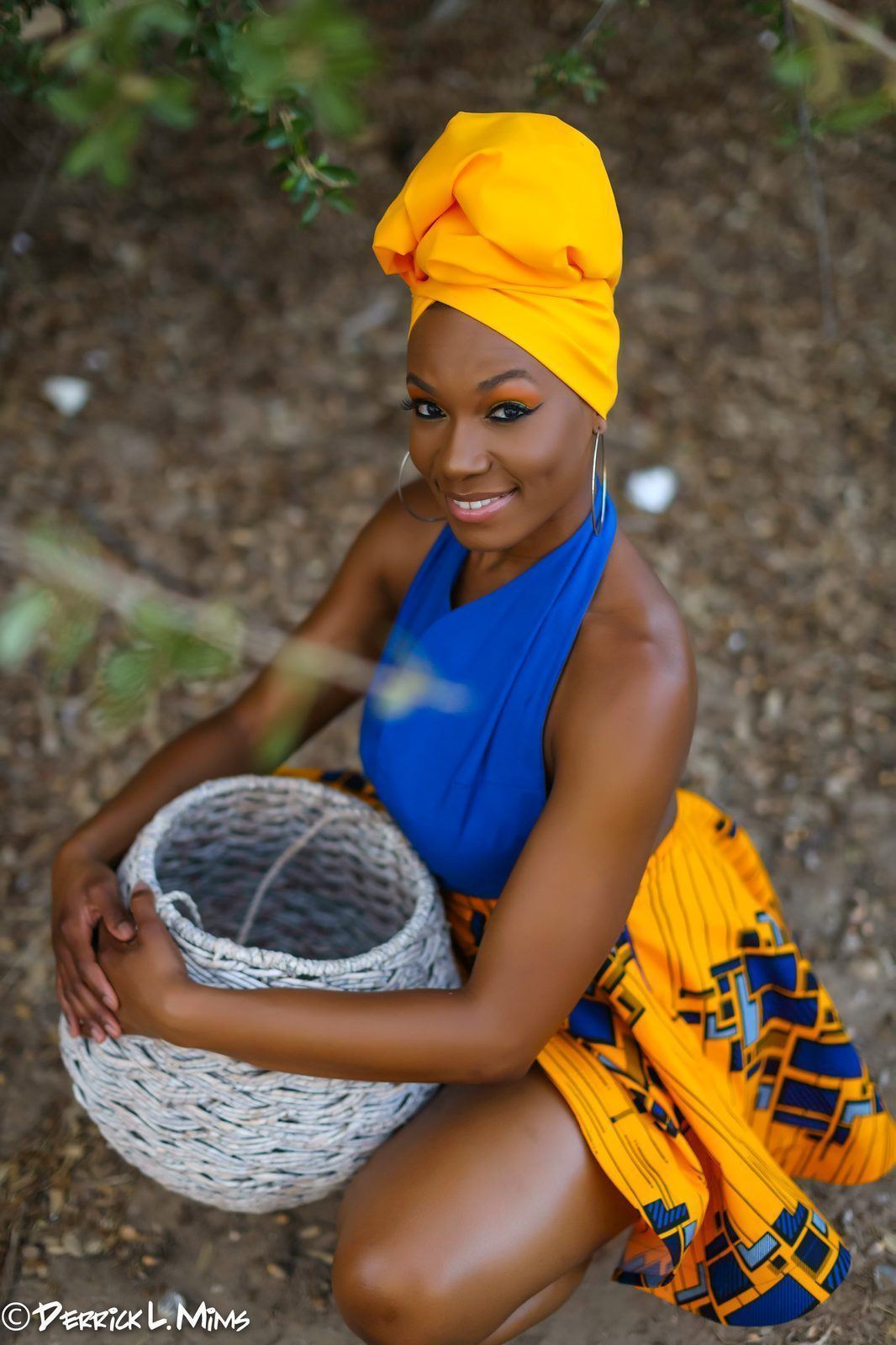 Photography — Model in a yellow head wrap and printed skirt kneeling outdoors with a woven basket, photographed from above