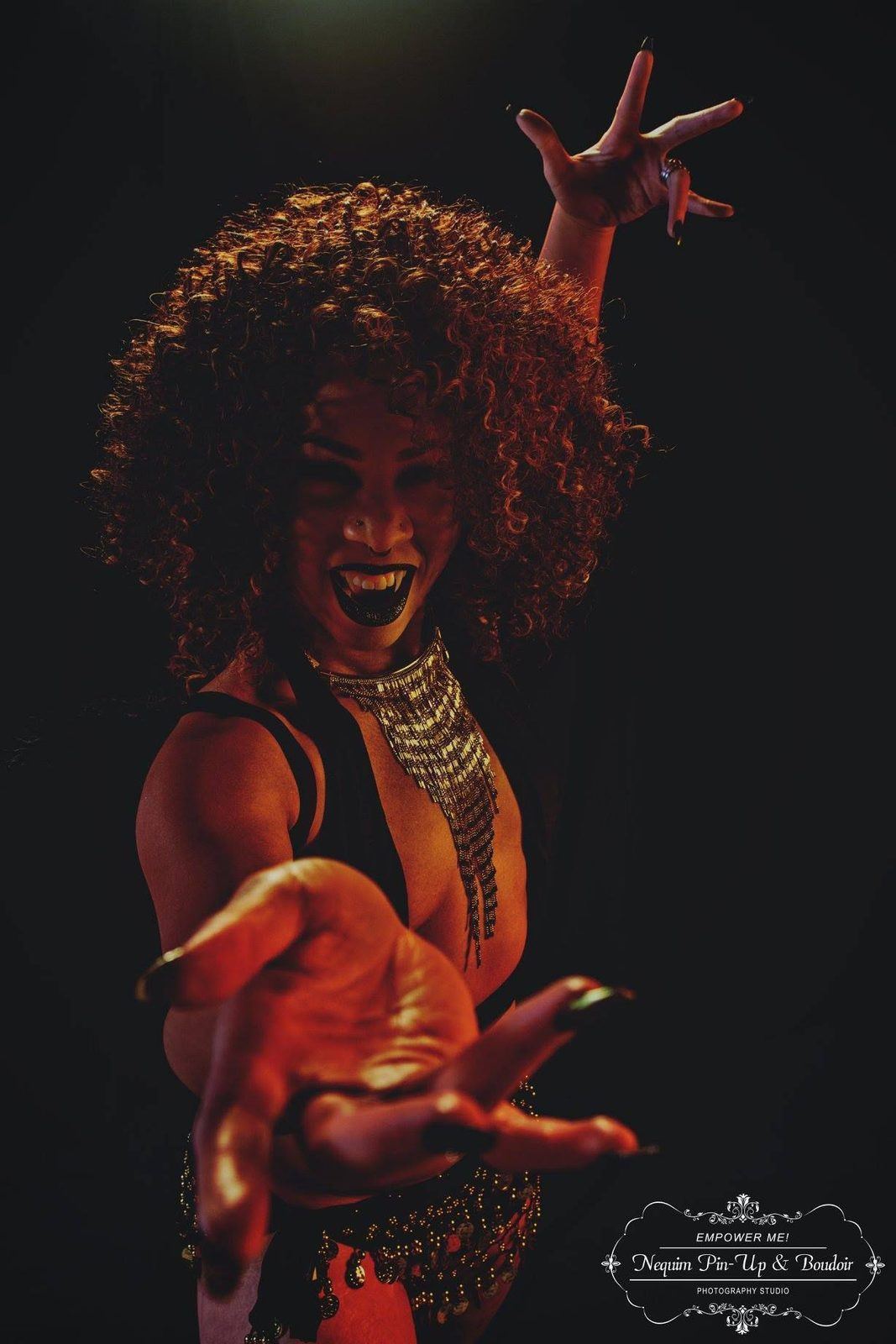 Photography — Theatrical low-light portrait of a model with vampire fangs and gold fringe necklace reaching toward the camera