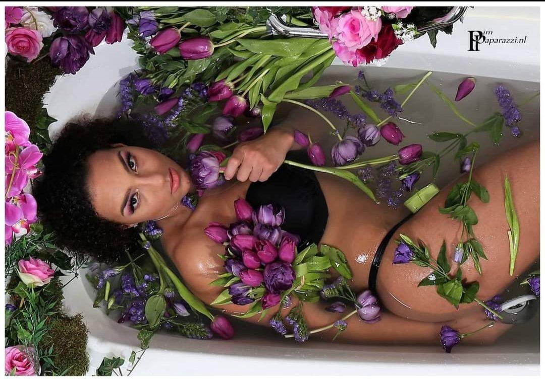 Photography — Model reclining in a bathtub filled with pink and purple flowers, photographed from overhead