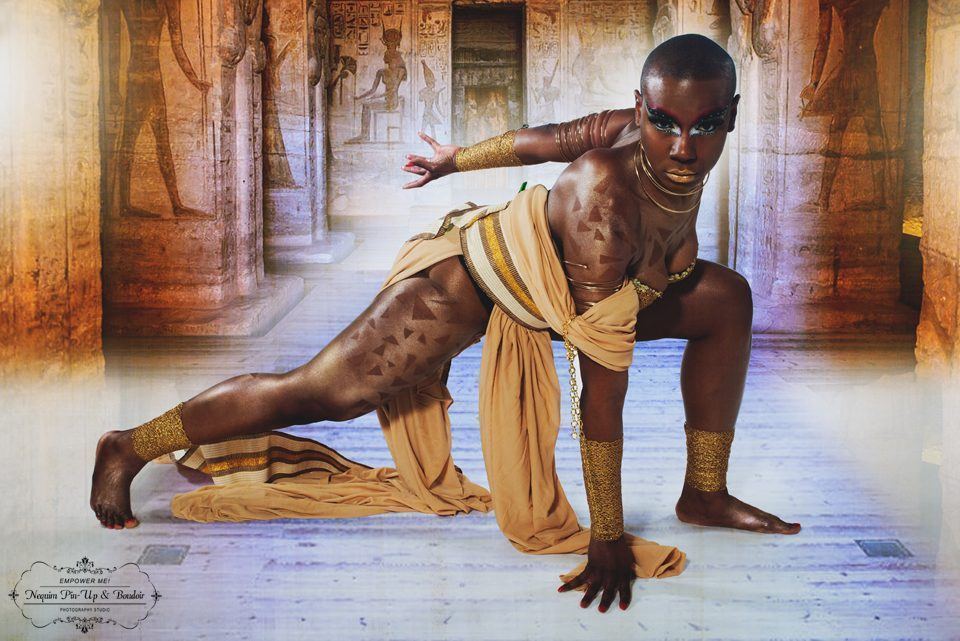 Photography — Model in gold body paint and draped fabric striking a low crouch against an Egyptian temple backdrop