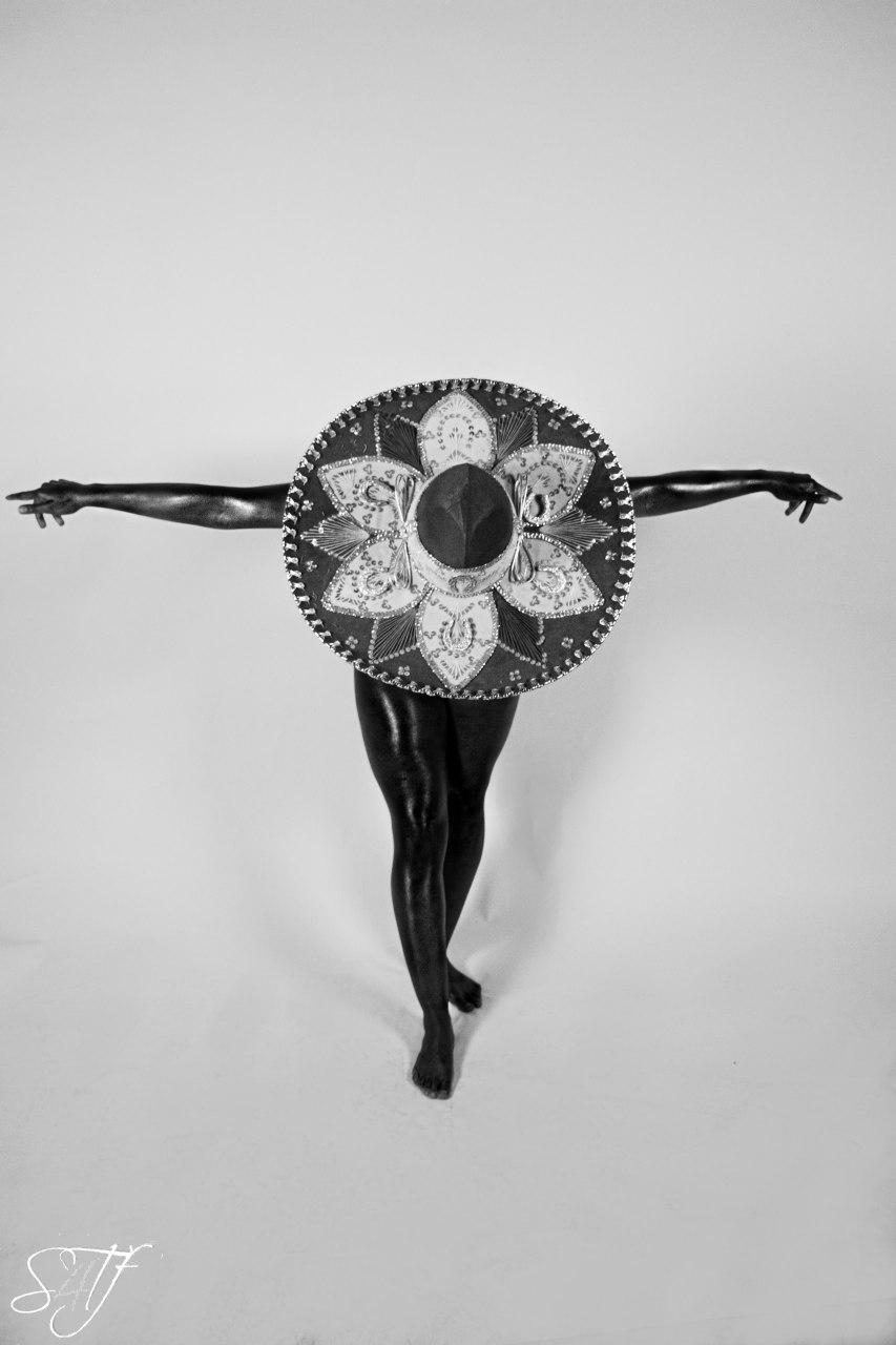 Photography — Black and white fine-art study of a model with arms outstretched, ornate sombrero concealing head and torso