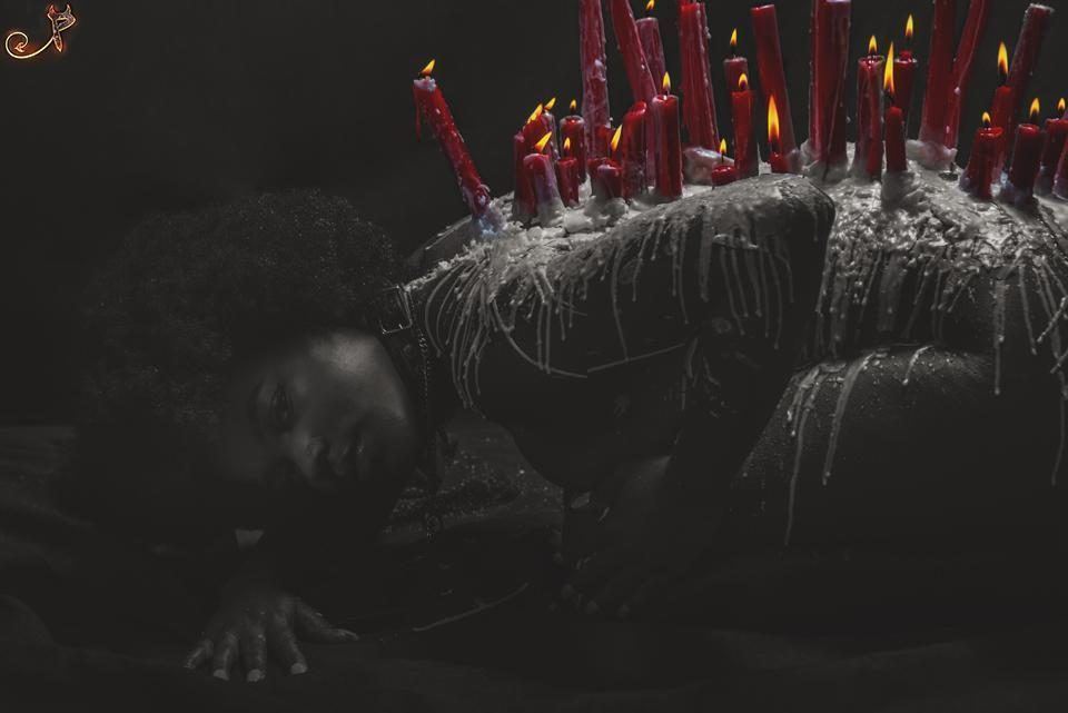 Photography — Dark conceptual portrait of a model kneeling with lit red candles and dripping wax along her back