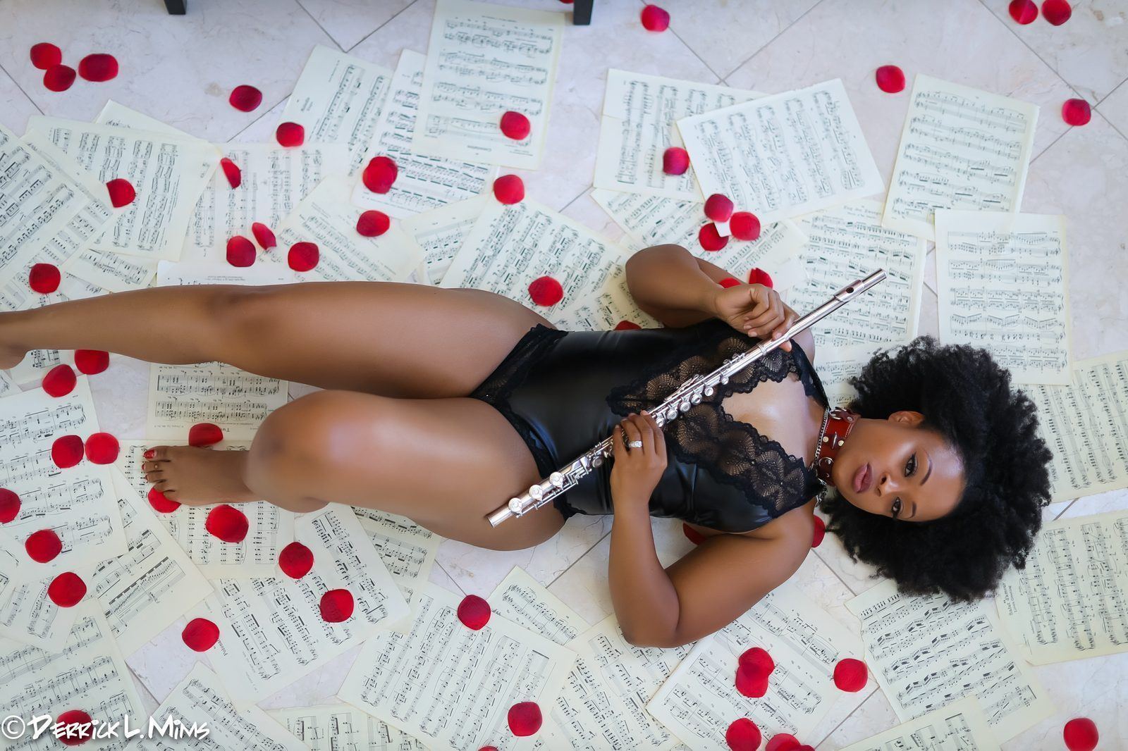 Photography — Overhead shot of a model in black lace holding a flute atop scattered sheet music and rose petals