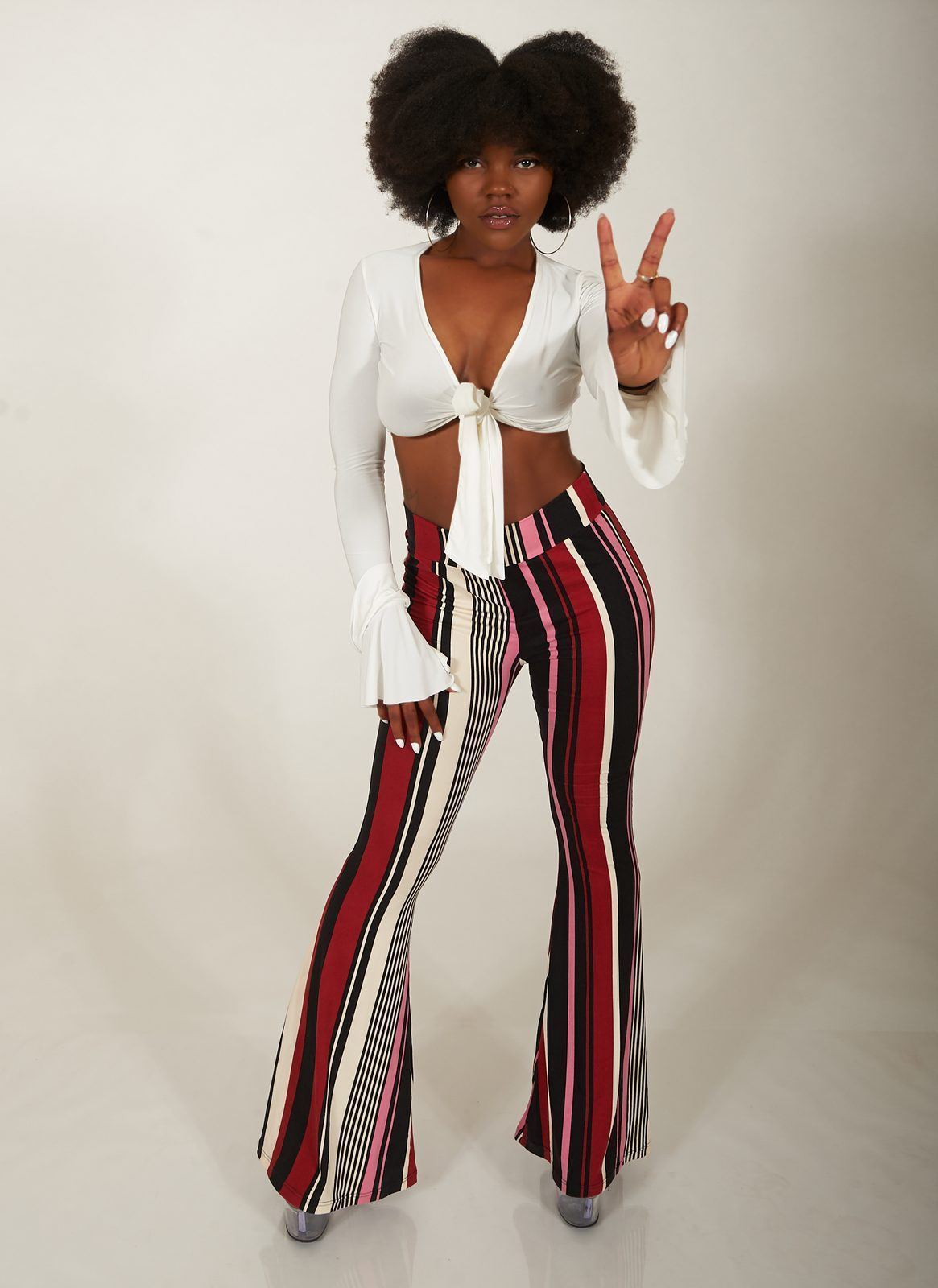 Photography — Model in a white tie-front top and striped flare pants flashing a peace sign in a studio